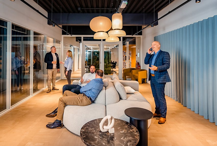 Mensen in gesprek en aan het werk in een moderne kantoorlounge met banken en warme verlichting.