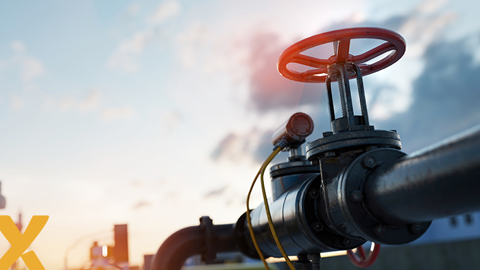 Close-up van een industriële gasleiding met afsluiter en rode klep bij zonsondergang.