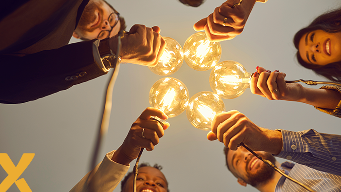 Groep mensen die samen brandende gloeilampen vasthouden als symbool voor samenwerking en ideeën.