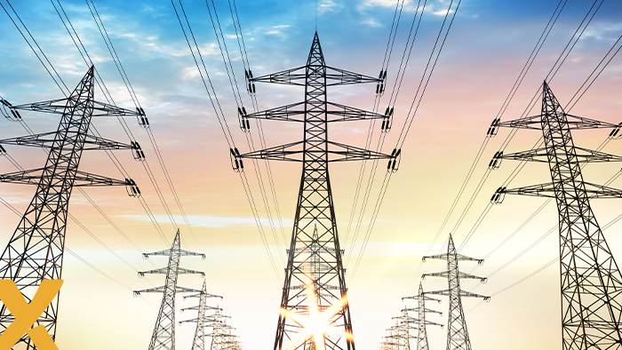 Rij hoogspanningsmasten met elektriciteitskabels tegen een kleurrijke zonsopkomst.