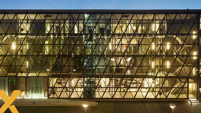 Modern kantoorgebouw met glazen gevel en opvallende driehoekige structuur, verlicht in de avond.