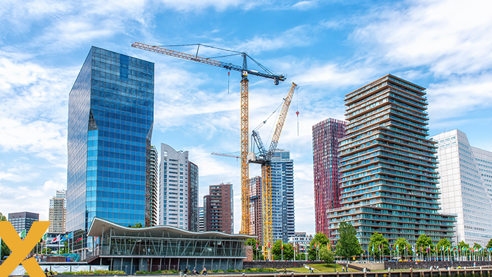 Moderne skyline met hoge kantoorgebouwen en bouwkranen aan het water onder een blauwe lucht.