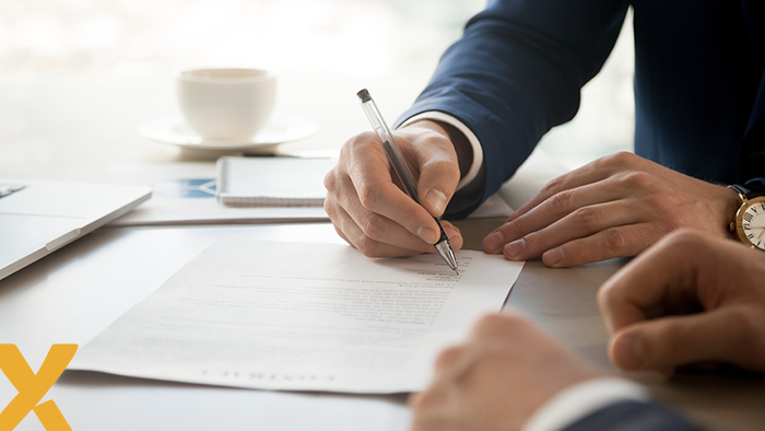 Persoon tekent een contract aan een bureau, met laptop en koffiekopje op de achtergrond