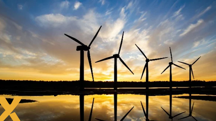 Windmolens bij zonsondergang weerspiegeld in het water, symbool voor duurzame energieopwekking.