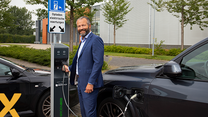 Man bij een laadpaal die een elektrische auto oplaadt op een parkeerplaats met EV-laadbord.