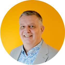 Portret van een lachende man in een lichtgrijs colbert voor een oranje achtergrond.