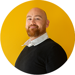 Portret van een man met baard, gekleed in een zwarte trui en witte kraag, poserend voor een gele achtergrond. Portret van een man met baard, gekleed in een zwarte trui en witte kraag, poserend voor een gele achtergrond.